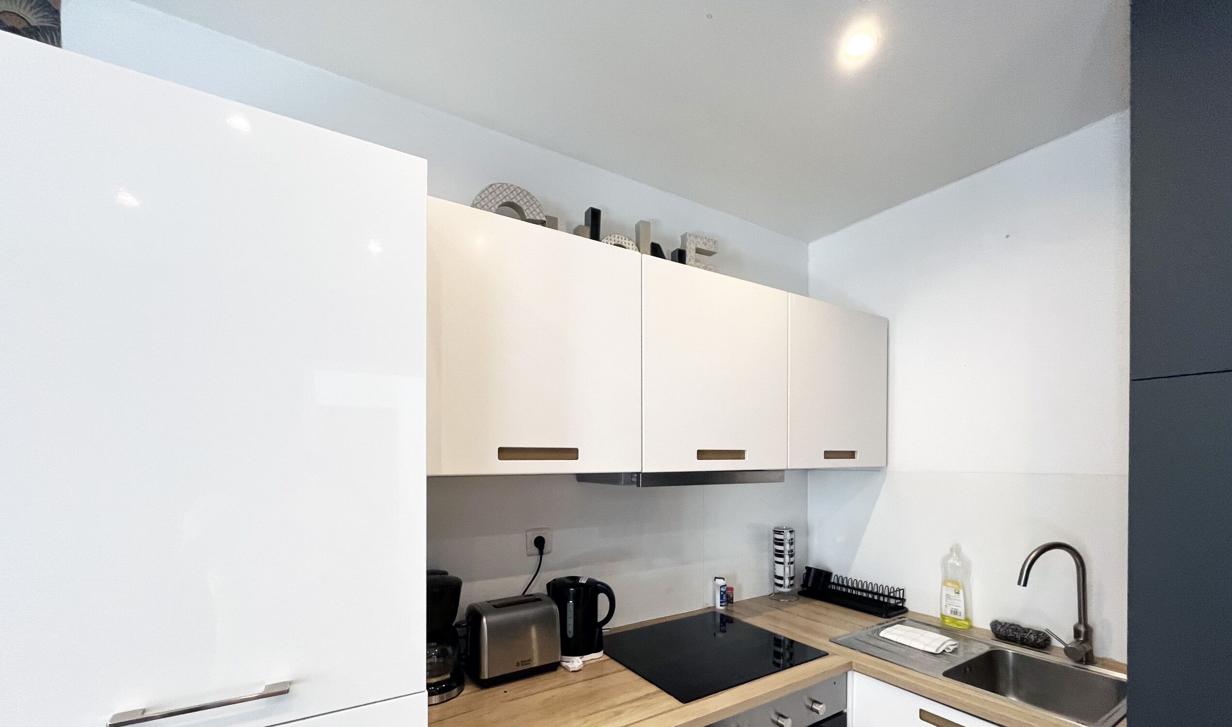 A modern kitchen with white cabinets, a black countertop, and a stainless steel sink.