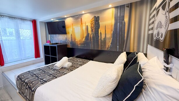 Ett modernt hotellrum med en stor säng, en platt-TV och en väggmålning som föreställer stadens skyline.
