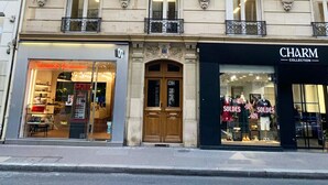 Um edifício com vários andares, com uma loja boutique no andar térreo chamada 'Charm Collection' e um restaurante com fachada de vidro.