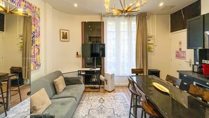 Uma sala de estar moderna com um sofá cinza, uma área de refeições com uma mesa preta e uma televisão grande.