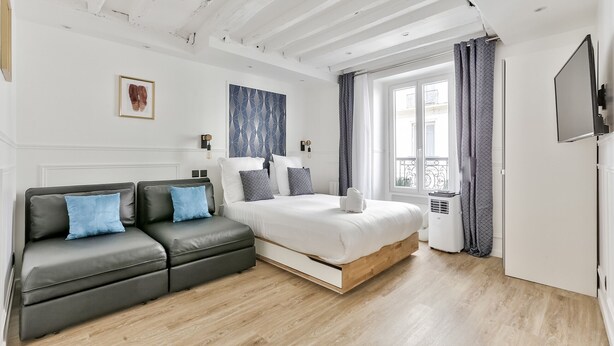 A modern bedroom with a bed, a sofa, a TV, and a window with curtains.