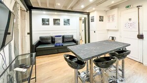 A modern interior with a marble table, black bar stools, a sofa with cushions, and framed pictures on the wall.