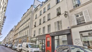 A row of parked cars along a street with buildings featuring storefronts, including a red door and a sign for 'VITRINE 65'.