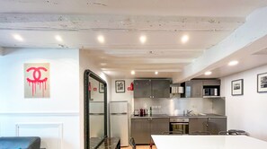Une cuisine moderne dotée d’appareils électroménagers en acier inoxydable, un coin repas avec une table et des chaises blanches, et un grand miroir.
