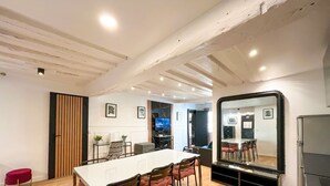 A modern dining area with a white table and chairs, a wooden slat partition, and a large mirror. - Urban Flat 100 - Pretty 2 Bedroom - Beaubourg Marais (París)
