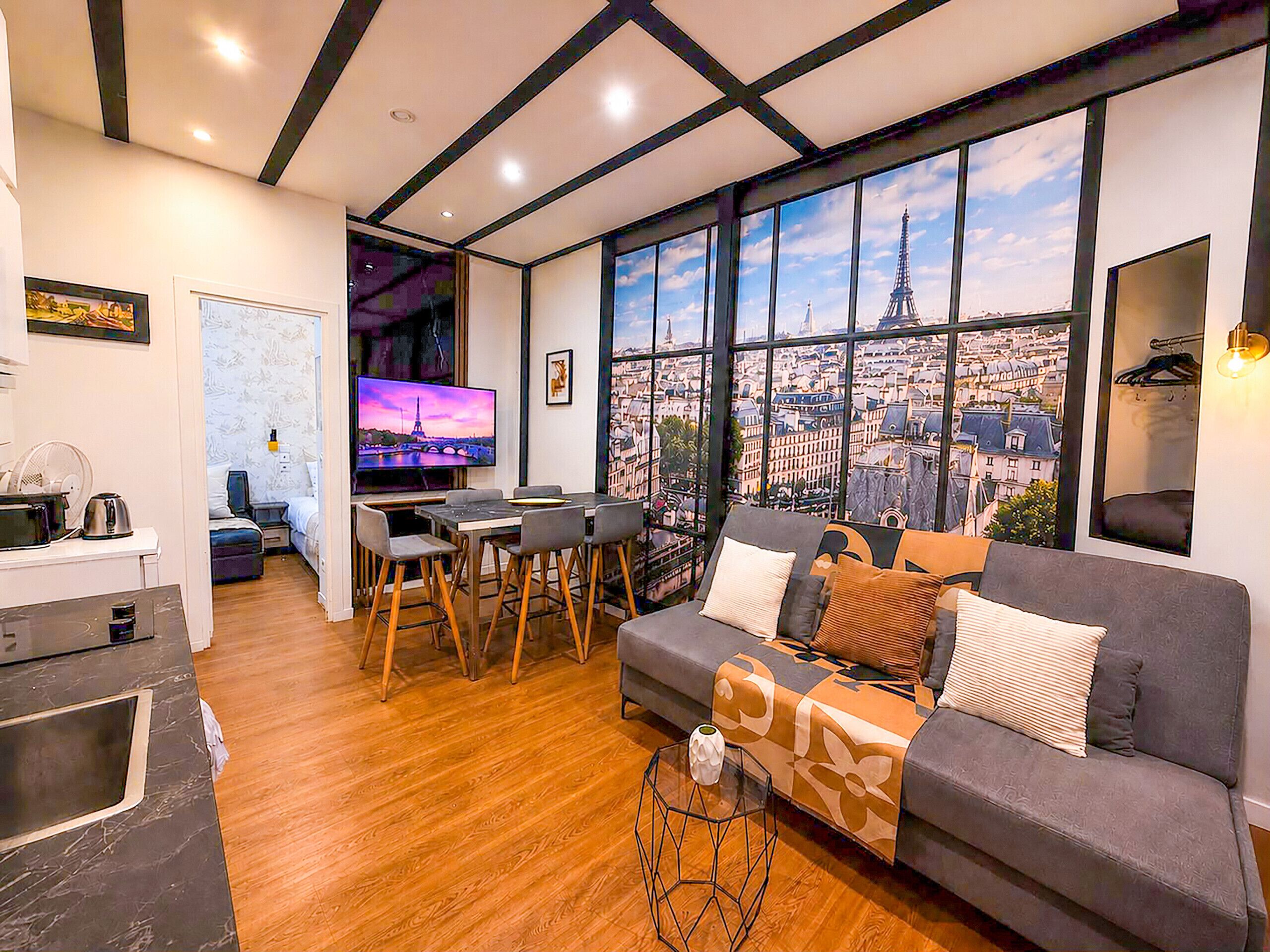 Een moderne woonkamer met een bank, een eettafel met stoelen, een televisie en een groot raam met uitzicht op de stad.