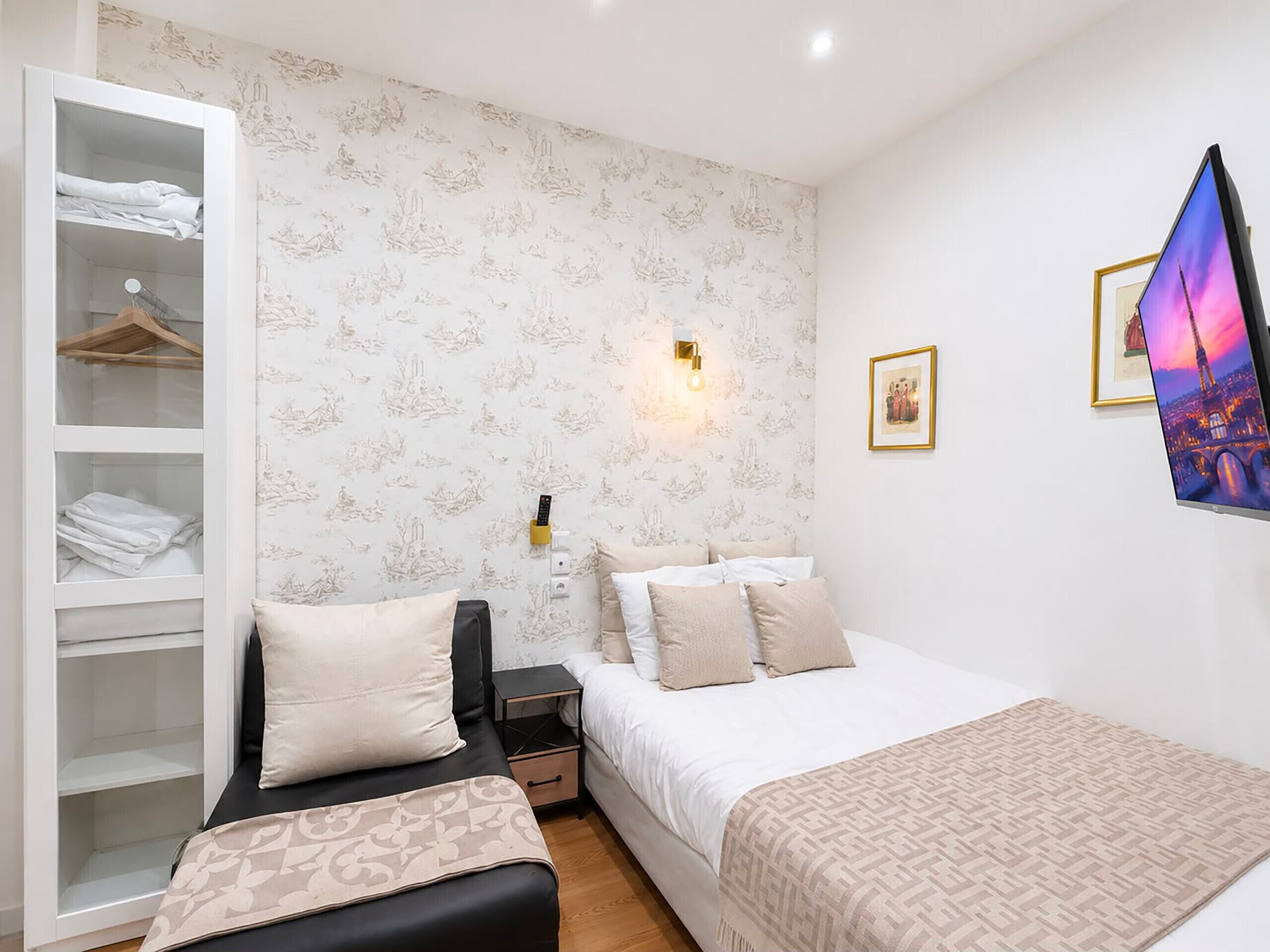 Ein Schlafzimmer mit einem Bett, Nachttischen, einem Kleiderschrank und einem an der Wand montierten Fernseher.