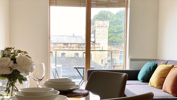 Ein Essbereich mit einem Tisch für vier Personen, einer Blumenvase und Blick auf Gebäude durch ein großes Fenster.