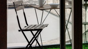 Blick von einem Balkon mit Tisch und Stuhl auf ein historisches Steinhaus und einen Baum.