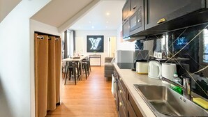 A modern kitchen with dark cabinetry, stainless steel appliances, and a large flat-screen TV mounted on the wall. - Urban Flat 115 A - Louis Fashion Apartment in Paris (París)