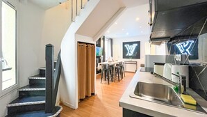A modern kitchen with a built-in dishwasher, a stainless steel sink, and a dining area with a table and chairs. - Urban Flat 115 A - Louis Fashion Apartment in Paris (París)