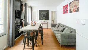 A modern living room with a dining area, a grey sofa, a TV, and artwork on the walls. - Urban Flat 115 A - Louis Fashion Apartment in Paris (París)