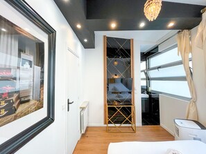 Ein modernes Hotelzimmer mit großem Fenster, integrierter Garderobe, Deckenleuchte und Heizkörper.