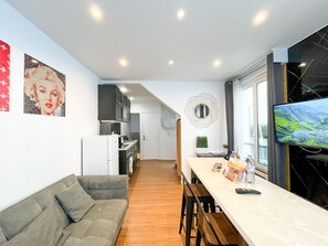 Eine moderne Küche mit weißen Geräten, ein Essbereich mit einem weißen Tisch und Stühlen sowie ein Fernseher auf der rechten Seite.
