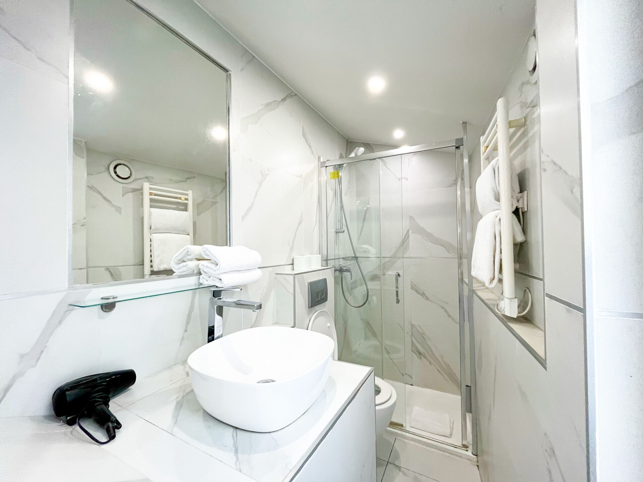 Een moderne badkamer met een douchecabine van glas, een witte wastafel en een handdoekhouder.
