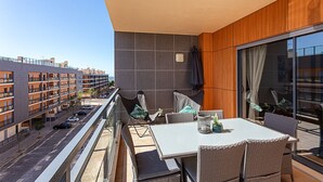 Ein Balkon mit Esstisch und Stühlen, Blick auf eine Stadtlandschaft und eine moderne Gebäudefassade.