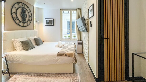 Un dormitorio con cama, reloj, televisor y ventana.