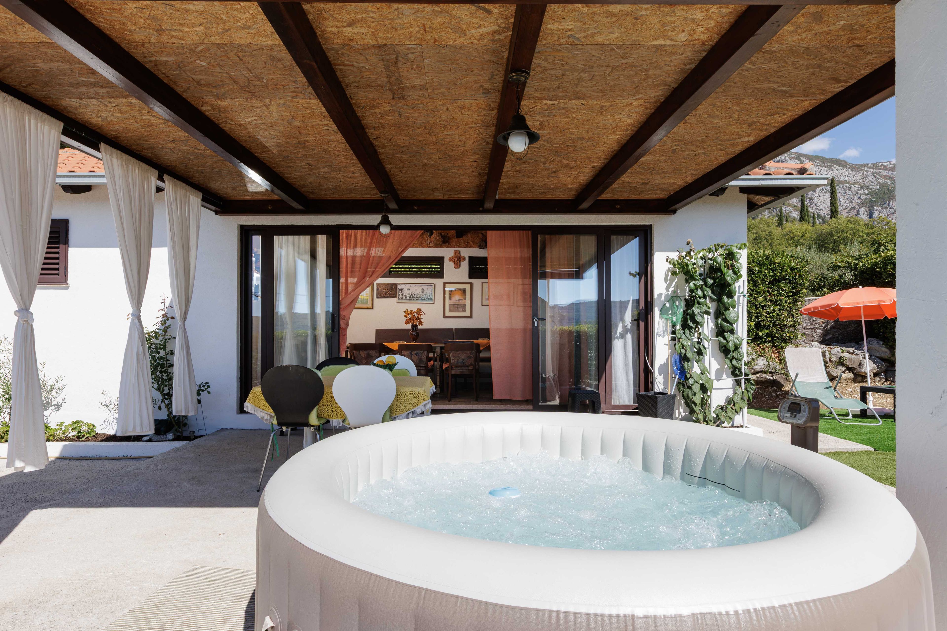 Un bain à remous situé dans un espace extérieur abrité, avec une table et des chaises visibles à travers une porte vitrée.