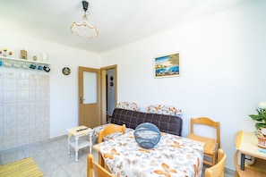 A room with a bed, a dining table with chairs, a small table with a bowl, a shelf with decorative items, and a painting on the wall. - Apartment Laurel Leaf (Konavle)