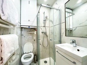 Un baño moderno con ducha de vidrio, inodoro blanco y lavamanos con espejo.