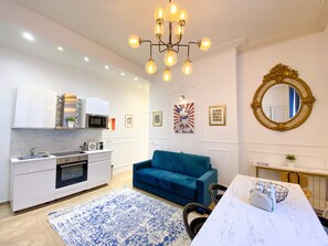 Une cuisine moderne avec des meubles blancs, un canapé bleu et un lustre.
