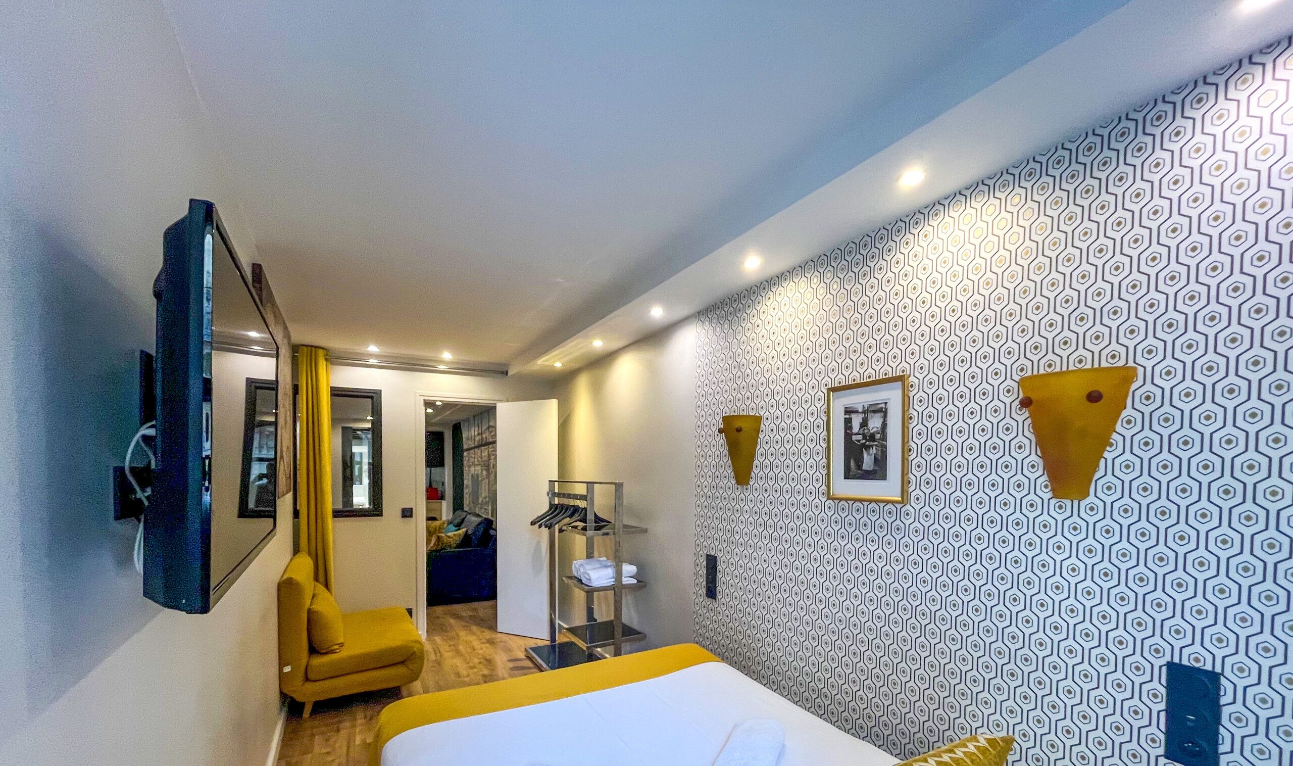Une chambre d’hôtel avec un lit, un miroir, une armoire et une salle de bain visible à travers une porte ouverte.
