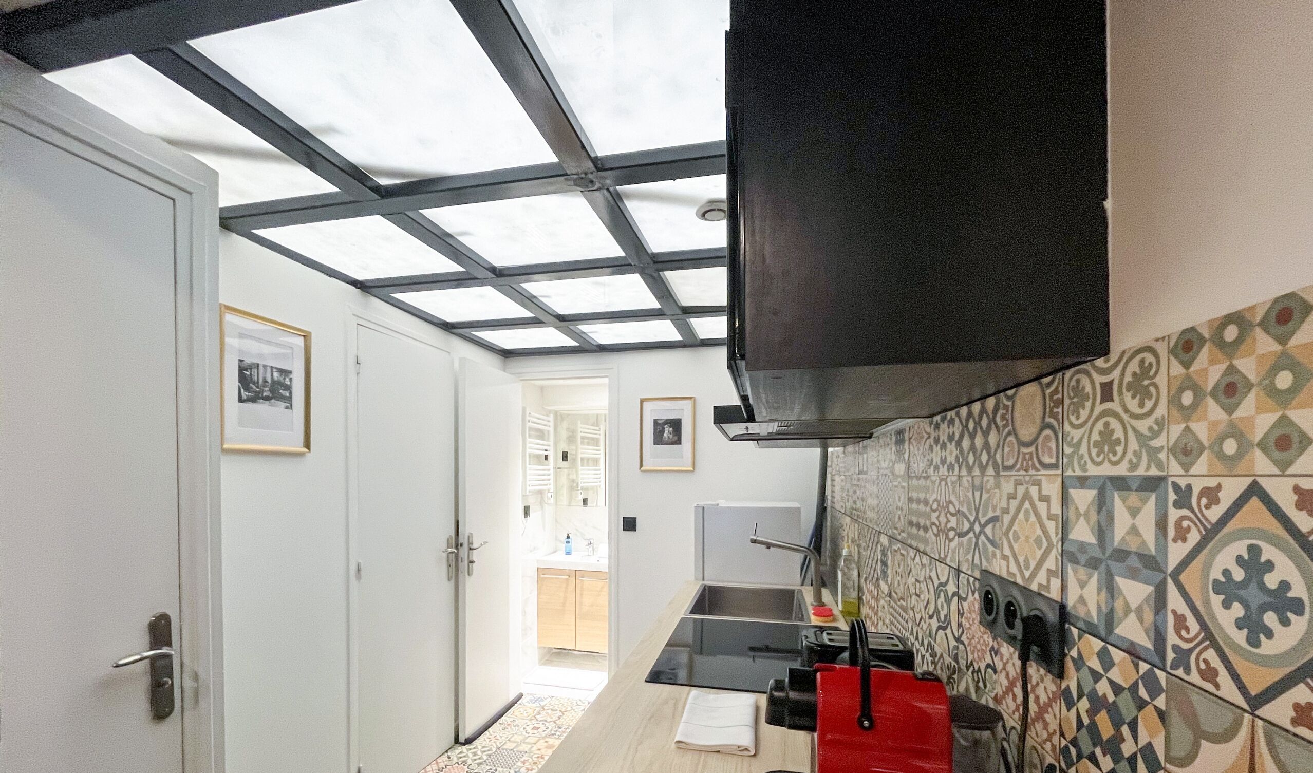 A narrow kitchen with a skylight, a black range hood, and patterned tiles.