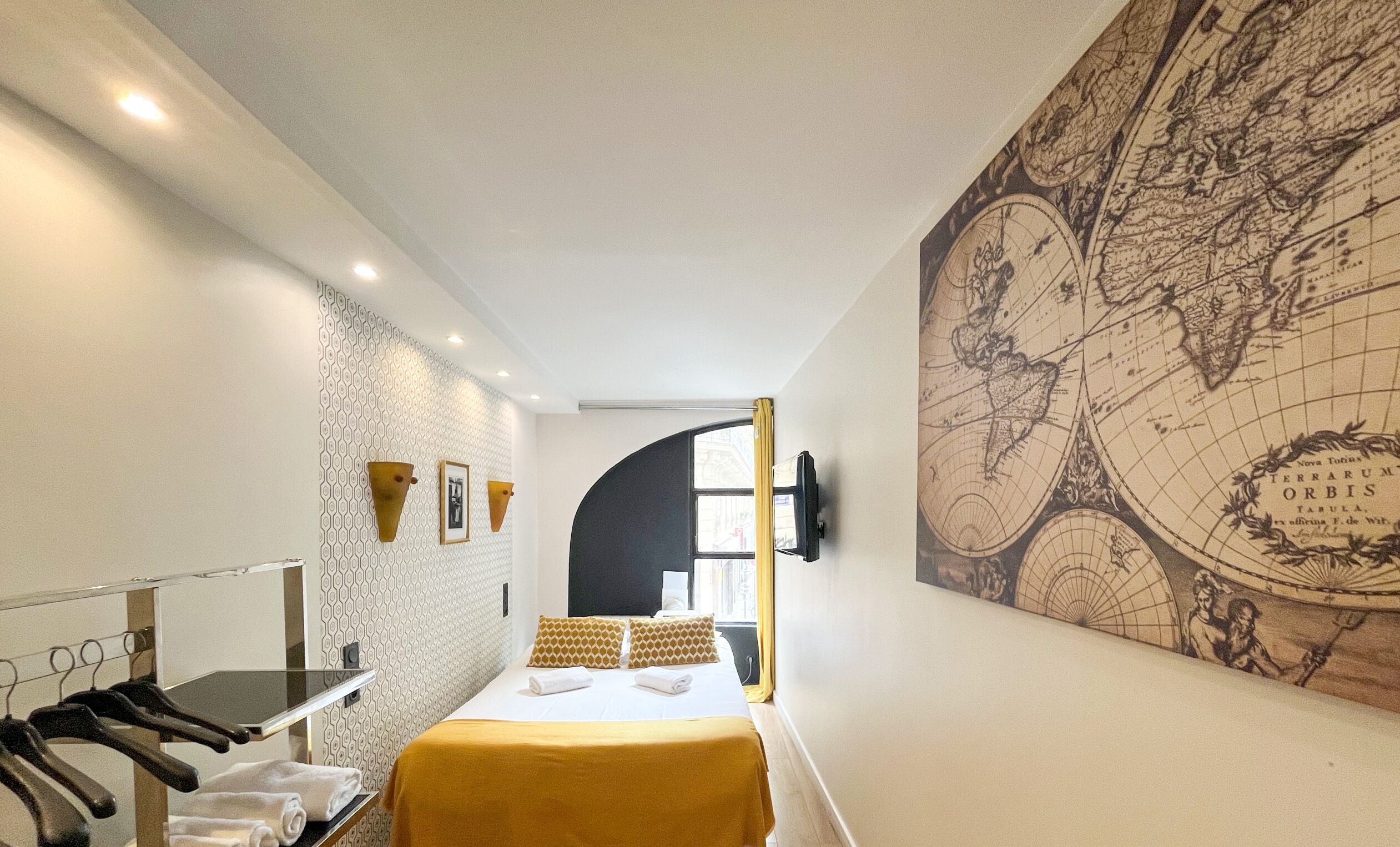 A hotel room with a bed, a map on the wall, a mirror, and a clothing rack.