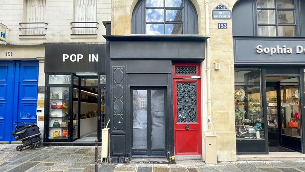 A storefront with a black door and a red door, and a sign that reads "POP IN".