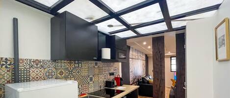 Una cocina moderna con encimera negra, salpicadero estampado y techo con tragaluces.