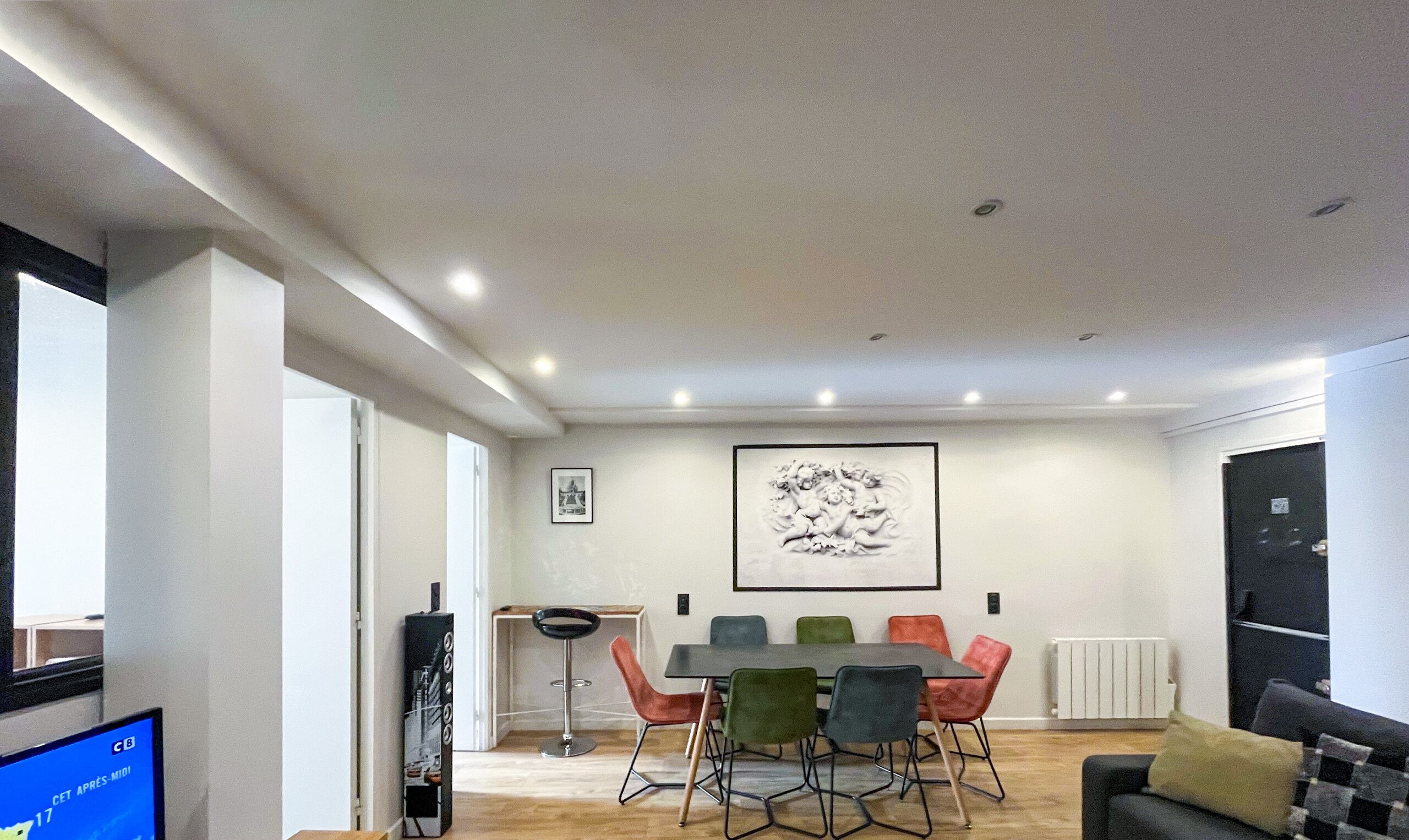 A modern living room with a dining area, a black sofa, a coffee table, and a TV on the left.