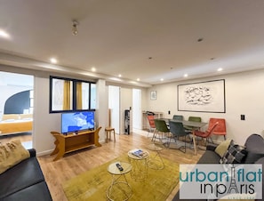 A modern living room with a TV, seating, a dining area, and artwork on the walls.