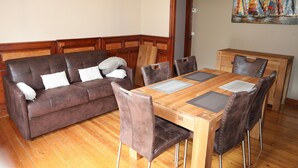 Een eethoek met een houten tafel, zes stoelen, een bruine bank en een schilderij aan de muur.