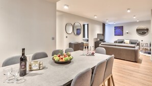 A modern dining area with a table set for two, a bottle of wine, and a fruit bowl.