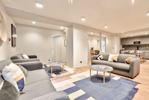 A modern living room with a grey sofa, two coffee tables, and a patterned rug.
