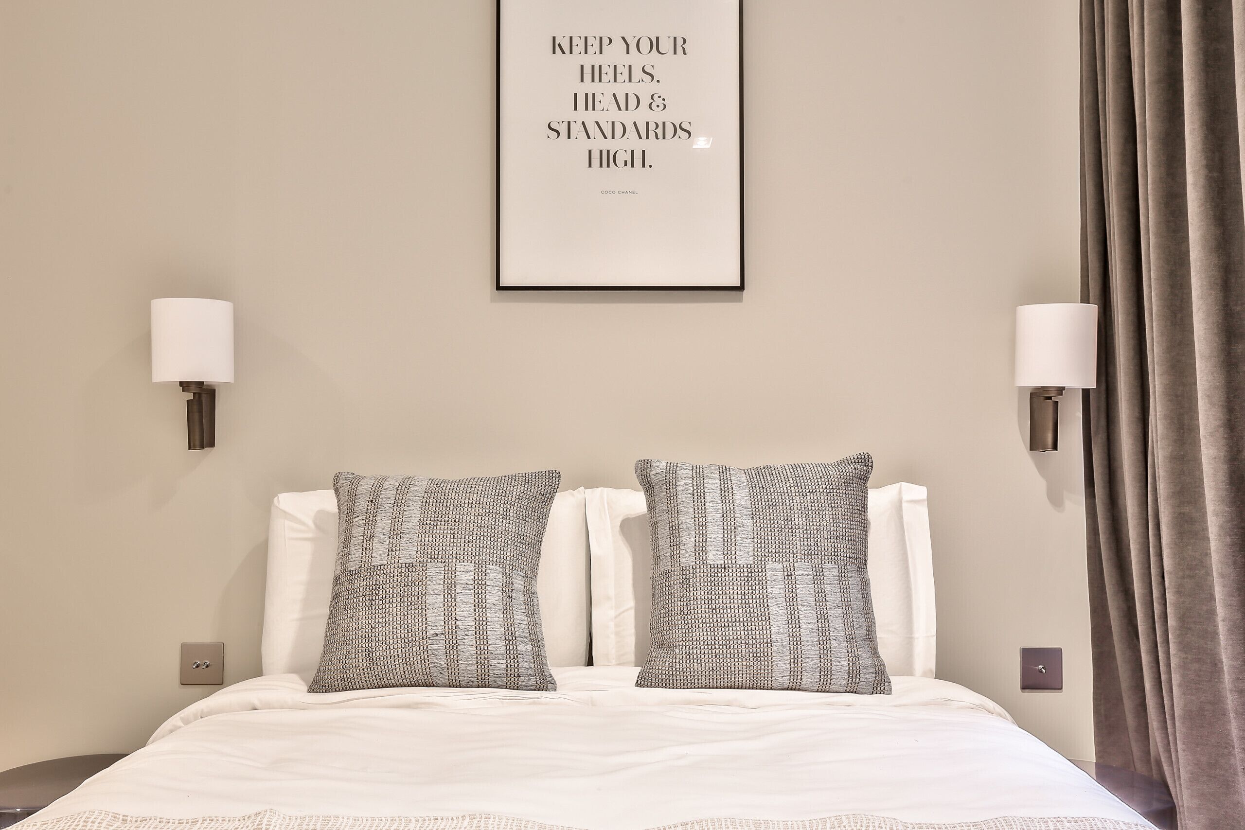 A neatly made bed with two patterned pillows, a framed inspirational quote on the wall, and a lamp on either side.