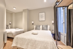 A hotel room with two beds, a large window with curtains, a wall-mounted light, and a motivational poster.