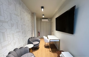 A modern room with a geometric patterned wall, a flat-screen TV, a white desk, and two leather armchairs.