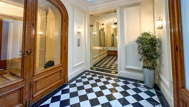 A hotel hallway with a checkered floor, a wooden door, and a skylight.