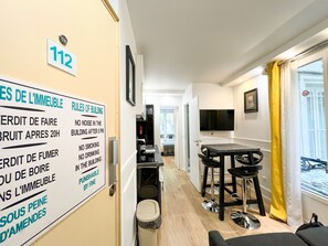Une chambre d’hôtel avec un coin repas, un téléviseur fixé au mur et une fenêtre avec un rideau jaune.