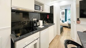 A compact kitchen with white cabinets, a black countertop, a microwave, and a stove.