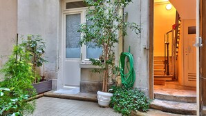 A small courtyard with a potted tree, a hose, and a door leading to a staircase.