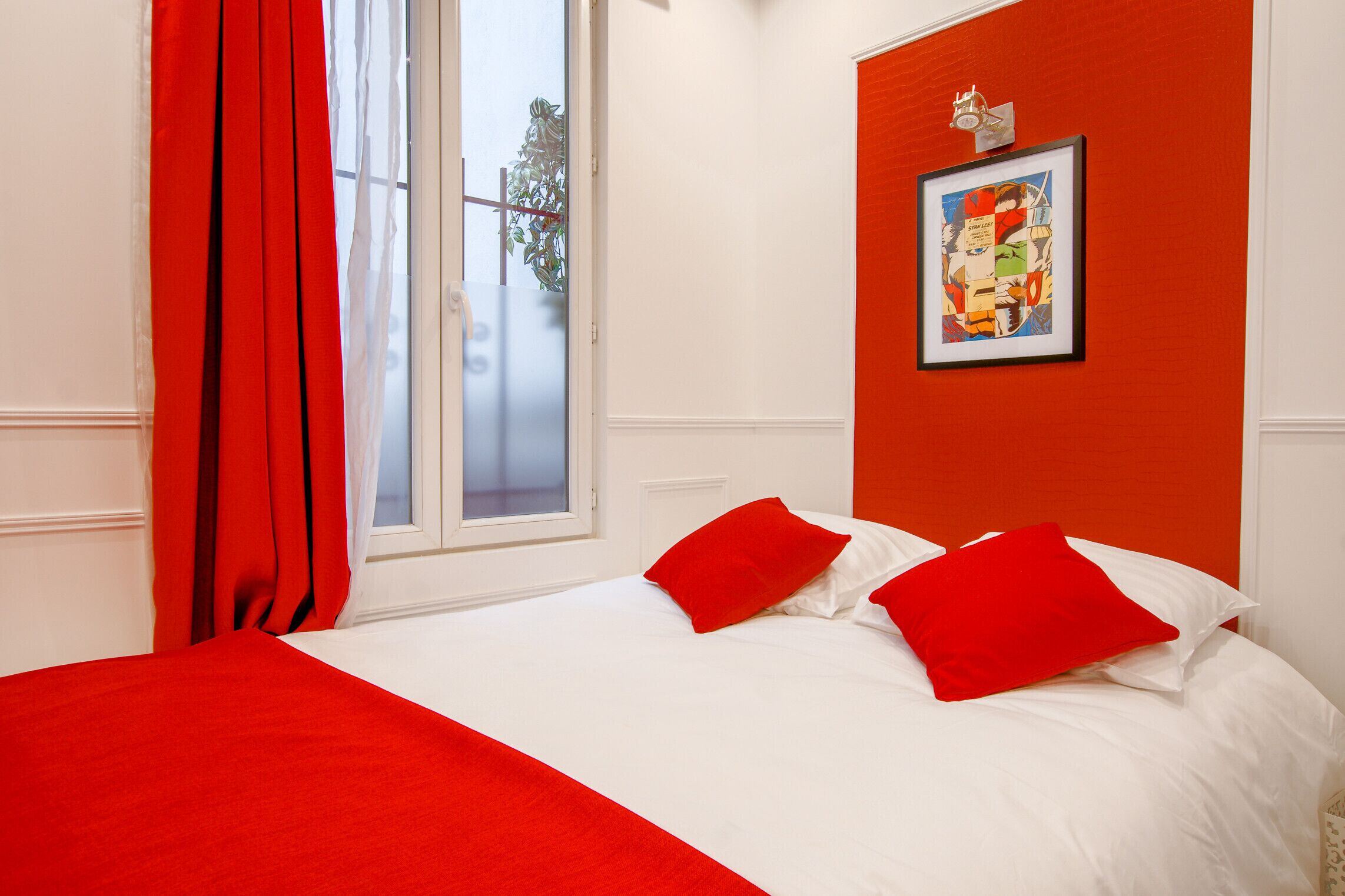Une chambre d’hôtel avec un lit, des rideaux rouges, une fenêtre donnant sur un beau paysage et un tableau encadré au mur.