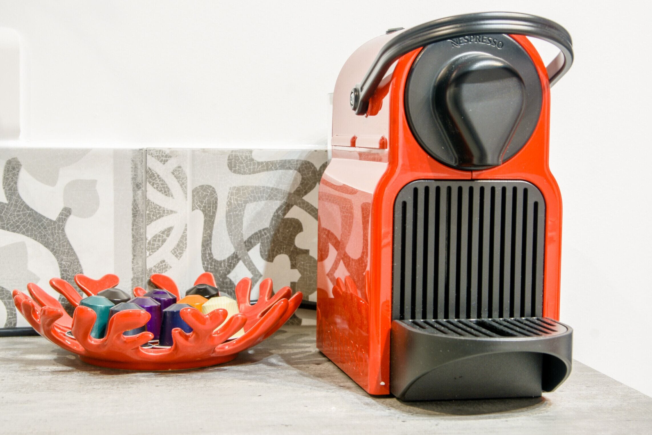 A red Nespresso machine next to a colorful, coral-shaped container holding various coffee pods.