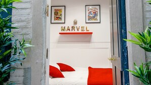 A bedroom with a white bed, red pillows, and a wall with Marvel comics and a 'MARVEL' sign.
