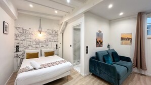 Un dormitorio moderno con cama, sofá azul, mural de paisaje urbano y una puerta que da a otra habitación.