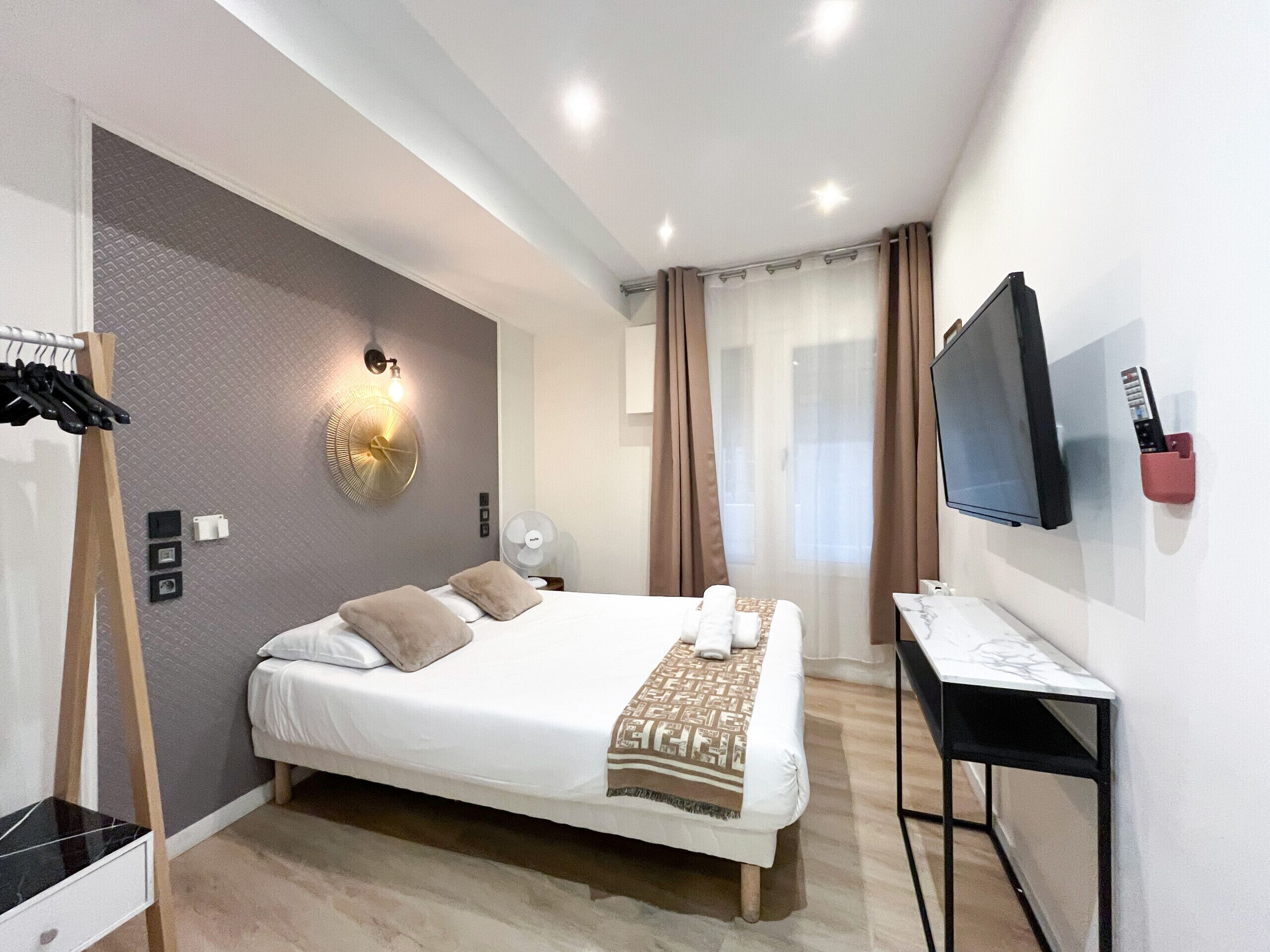 Una habitación de hotel moderna con una cama grande, un escritorio, un televisor y un ventilador de pared.