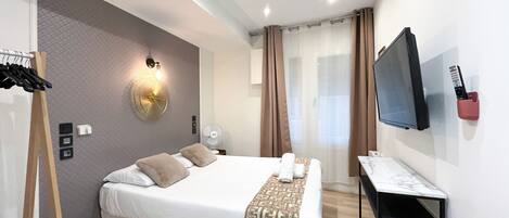 Una habitación de hotel moderna con una cama grande, un escritorio, un televisor y un ventilador de pared.
