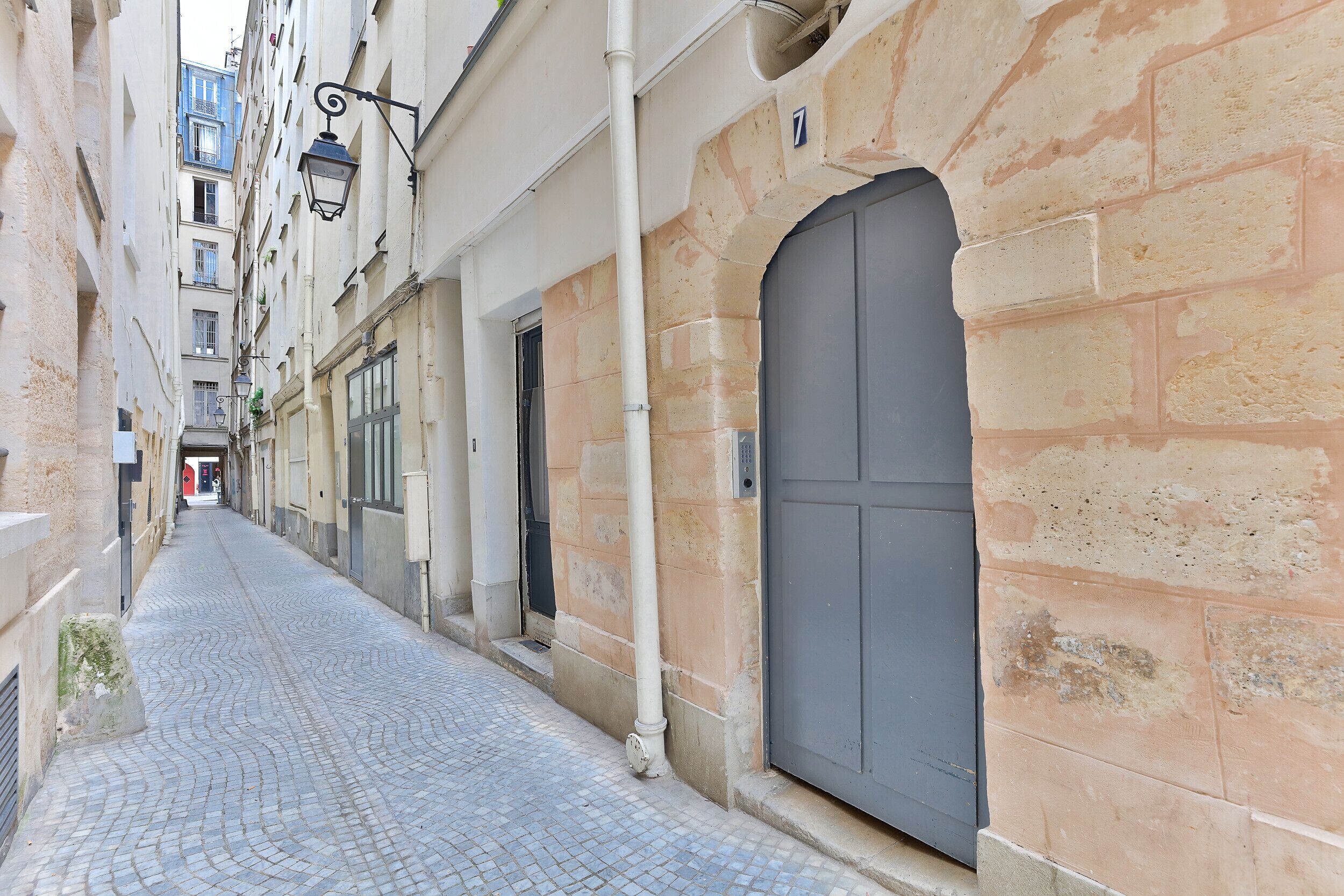 A narrow cobblestone street flanked by buildings with stone facades and a large grey door.