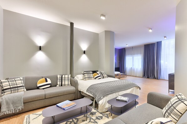 A modern hotel room with a sofa, a bed, a small table, and a TV.